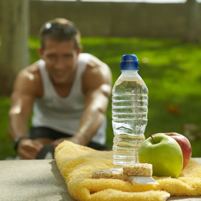 sports nutrition - man stretching with water, fruits, and fit bar in front of him