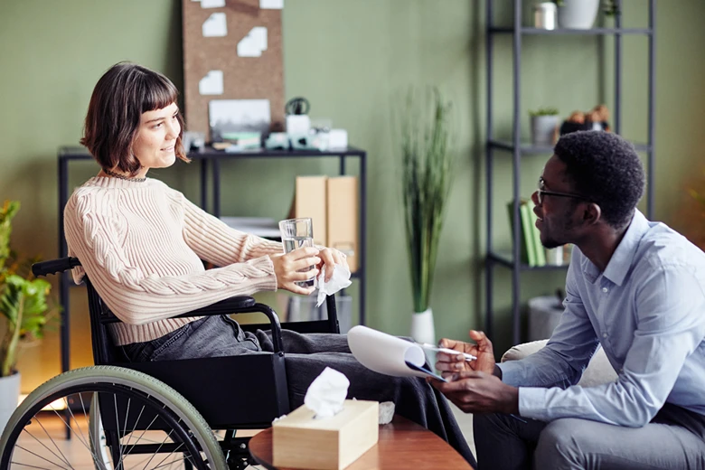 A man in a wheelchair engages in conversation with a woman, both smiling and appearing attentive to each other.
